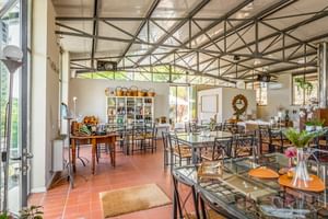 Bright restaurant interior at Le Valli Agriturismo in Casciana Terme with metal-framed ceiling, terracotta floors, glass-topped tables and shelving.