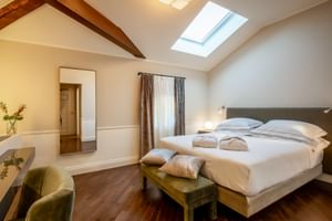 Helles Doppelzimmer mit Holzbalken, Dachfenster, Doppelbett, Holzbank, Schreibtisch mit Stuhl und Tür zum Bad in Villa Soligo.