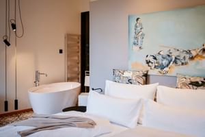 Modern hotel room with white bed, freestanding bathtub, artistic headboard, and pendant lights at Landhaus zu Appesbach.