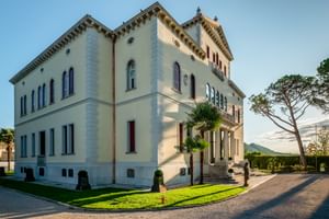 Elegante neoklassizistische Villa Soligo in Farra di Soligo mit cremefarbener Fassade, Ziergesimsen und Bogenfenstern. Palmen und gepflegter Rasen davor.