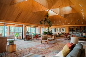 Spacious lounge with geometric wooden ceiling, colorful patterned rug, modern furniture, and large windows overlooking nature at FeelViana Sport Hotel.