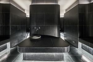 Moderne Dampfsauna im The Dean München mit schwarzen Fliesen, zentraler beheizter Plattform, geschwungenen Wänden und Ambientebeleuchtung.