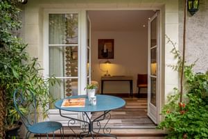 Private Terrasse mit blauem Metalltisch und Stuhl im Auberge du Bon Laboureur in Chenonceaux, mit offenen Flügeltüren zu einem Zimmer.