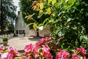Rosa Begonien im Vordergrund mit Kiesterrasse, weißen Gartenmöbeln und historischem Steingebäude im Le Grand Monarque in Azay-le-Rideau.