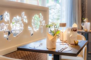 Eleganter Restauranttisch im Gartenhotel Heusser Bad Dürkheim mit beleuchteter floraler Wanddekoration, Orchidee und Gedeck.