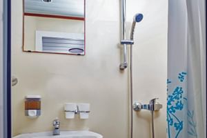Compact bathroom on MS Macek ship with white sink, mirror, shower with curtain, and chrome fixtures on cream walls.