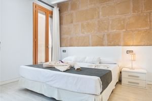 Modern double room with white bed, natural stone wall, wooden door, white nightstand with lamp, and light wooden flooring.