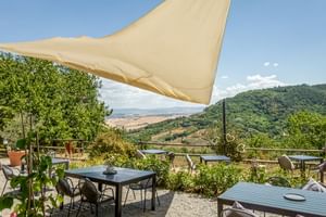 Outdoor terrace with tables and chairs under beige sun sail at Le Valli Agriturismo in Casciana Terme, overlooking rolling Tuscan hills.