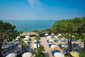 Beach terrace with blue sun loungers and striped umbrellas at Hotel Du Lac et Bellevue in Bardolino, overlooking Lake Garda.