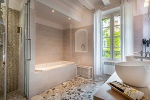 Elegantes Badezimmer mit beigen Fliesen, weißer Badewanne, Glasdusche, Standwaschbecken und Terrazzoböden im Auberge du Bon Laboureur in Chenonceaux.
