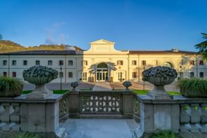 Villa Soligo in Farra di Soligo mit cremefarbener Fassade und Bogeneingang. Steinbalustrade mit Zierurnen rahmt die Abendansicht.