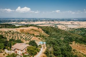 Aerial view of Le Valli Agriturismo in Casciana Terme with stone farmhouse, pool, and rolling Tuscan hills with olive groves and fields.