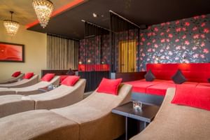 Eleganter Ruheraum mit beigen Liegen mit roten Kissen, roter Sofaecke, Kristalllüstern und dunkler Blumentapete mit roten Akzenten.