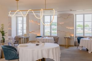 Elegant restaurant interior at Fleur de Loire Blois with white tablecloths, blue velvet chairs, artistic wave lighting, and decorative wall elements.
