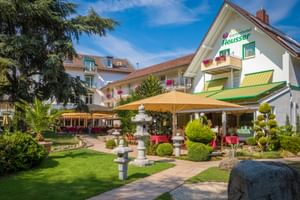 Gartenhotel Heusser in Bad Dürkheim mit weißer Fassade, grünen Markisen, Terrasse mit gelben Sonnenschirmen und Garten mit asiatischen Steinlaternen.