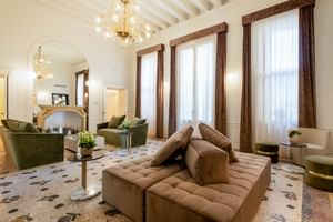 Eleganter Eingangsbereich der Villa Soligo mit Balkendecke, Murano-Kronleuchter, Terrazoboden, braunem Sofa und grünen Sesseln.