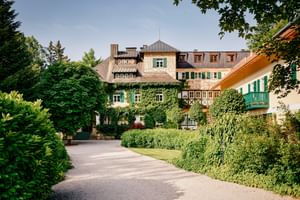 Landhaus zu Appesbach with ivy-covered facade, green shutters, and manicured gardens. A gravel driveway leads to the traditional Austrian building.