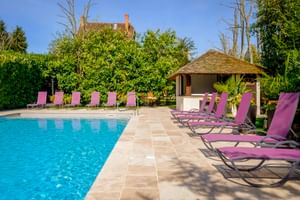 Außenpool im Auberge du Bon Laboureur in Chenonceaux mit lila Liegen, strohgedecktem Poolhaus und üppigem Garten unter blauem Himmel.