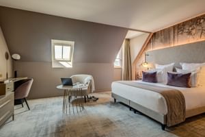 Modern attic double room with sloped ceiling, skylight window, gray upholstered bed, seating area, and wooden beam accent wall at Hotel Fleur de Loire.