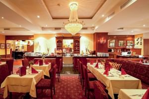 Elegantes Restaurant mit weiß gedeckten Tischen, roten Polsterstühlen, Kristallleuchter und Buffetbereich mit Holzschränken.