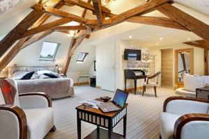 Geräumige Dachgeschoss-Suite mit sichtbaren Holzbalken, weißen Böden, Schlafbereich, Sitzgelegenheit und Bad im Auberge du Bon Laboureur.