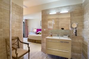 Modernes Bad mit beigen Fliesen und Waschtisch, offen zum Schlafzimmer mit Doppelbett im Auberge du Bon Laboureur in Chenonceaux.