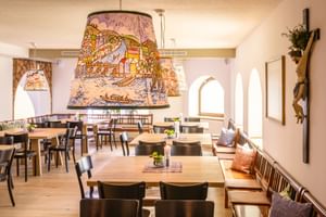 Heller Speisesaal mit Holztischen, dunklen Stühlen und dekorativen Lampenschirmen mit bunten Illustrationen im Hotel Post Traunkirchen.