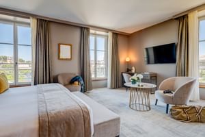 Elegant double room at Hotel Fleur de Loire Blois with large bed, beige armchairs, wall-mounted TV, and French windows overlooking the city.