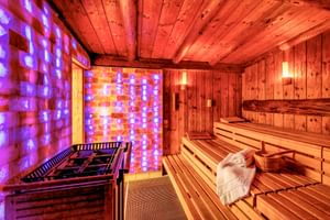 Finnische Holzsauna mit Sitzbänken, Saunaofen und beleuchteten Salzsteinwänden in lila und orange Licht im Gartenhotel Heusser.