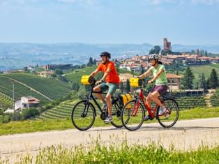 Zwei Radfahrer auf einem Radweg mit Montforte und Weinbergen im Hintergrund