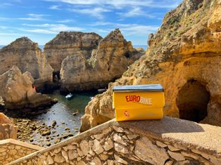 A yellow pannier on a stone parapet, rock formations and a cave on the coast in the background