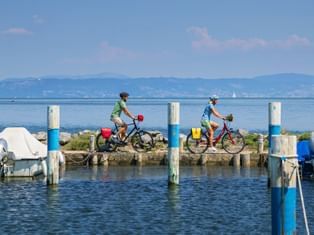 Two cyclists ride along the harbour in Grado