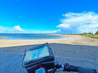 Blick auf die Tourenkarte in der Fahrradlenkertasche, im Hintergrund Sandstrand und Meer