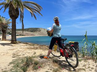 Radfahrerin beim Lesen der Reiseunterlagen an einem schönen Strand mit Palmen