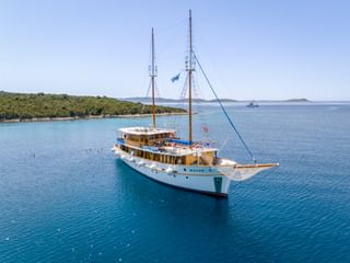 Weißes Motorsegelschiff MS Macek mit zwei Masten vor Anker in türkisfarbenem Adriatischem Meer nahe grüner kroatischer Küste.