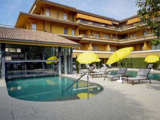 Yellow hotel building with balconies and outdoor pool area with sun loungers and yellow umbrellas at Du Lac et Bellevue in Bardolino.