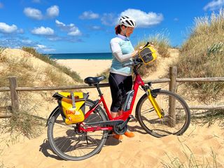 Cyclist standing on beach in Algarve with her bike