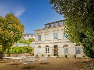 Elegantes cremefarbenes Herrenhaus Le Grand Monarque in Azay-le-Rideau mit Bogenfenstern und Außenterrasse mit weißen Tischen und Stühlen.
