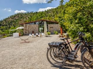 Stone building with terrace and white sun loungers at Agriturismo Le Valli in Casciana Terme. Bicycles parked on gravel courtyard, hills in background.
