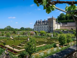Château de Villandry with formal French gardens featuring geometric hedges, topiary trees, and ornamental patterns under a blue sky.