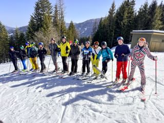 Gruppe von Skifahrern in bunter Winterkleidung posiert auf verschneiter Piste mit Wald und Bergen im Hintergrund beim Eurofun Touristik Wintersporttag 2026.