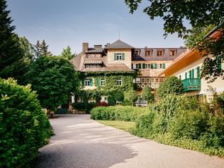 Landhaus zu Appesbach with ivy-covered facade, green shutters, and manicured gardens. A gravel driveway leads to the traditional Austrian building.