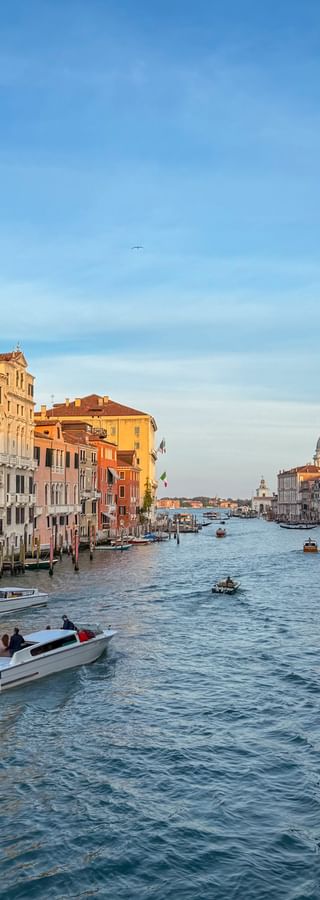 View along Venice's Canal Grande with boats, historic palaces lining both sides, and the dome of Santa Maria della Salute church in the distance.