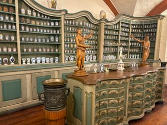 Innenraum des Heidelberger Apothekenmuseums mit geschwungenen Regalen voller antiker Keramikgefäße, Holztheke mit Schubladen und goldenen Statuen.