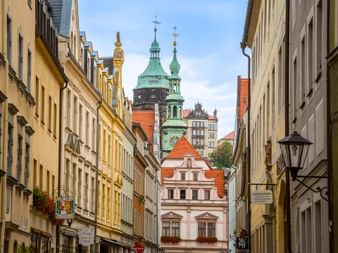 Enge Gasse in der Görlitzer Altstadt mit bunten historischen Gebäuden und Blick auf Kirchtürme mit grünen Kupferkuppeln und orangen Dächern.