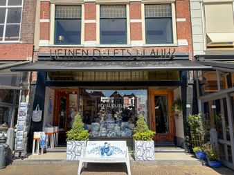 Ladenfront von Heinen Delfts Blauw in Delft mit blau-weißer Delfter Keramik in den Schaufenstern und dekorativen Pflanzgefäßen am Eingang.