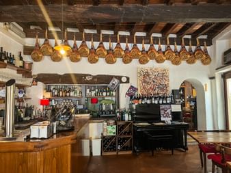 Traditionelles Weinbar-Interieur im Friaul mit einer Reihe luftgetrockneter Schinken an Holzbalken. Bartheke und Weinpräsentation unter rustikaler Decke.