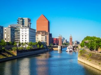 Duisburg Inner Harbor with canal, modern buildings including distinctive orange triangular structure, and boats moored along waterway.