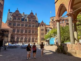 Besucher im Innenhof des Heidelberger Schlosses mit prächtigem Renaissancepalast und Steinbogen unter blauem Himmel.