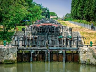 Historische Schleusentreppe Fonseranes am Canal du Midi bei Béziers mit Metalltoren, Steinmauern und grünen Böschungen unter bewölktem Himmel.